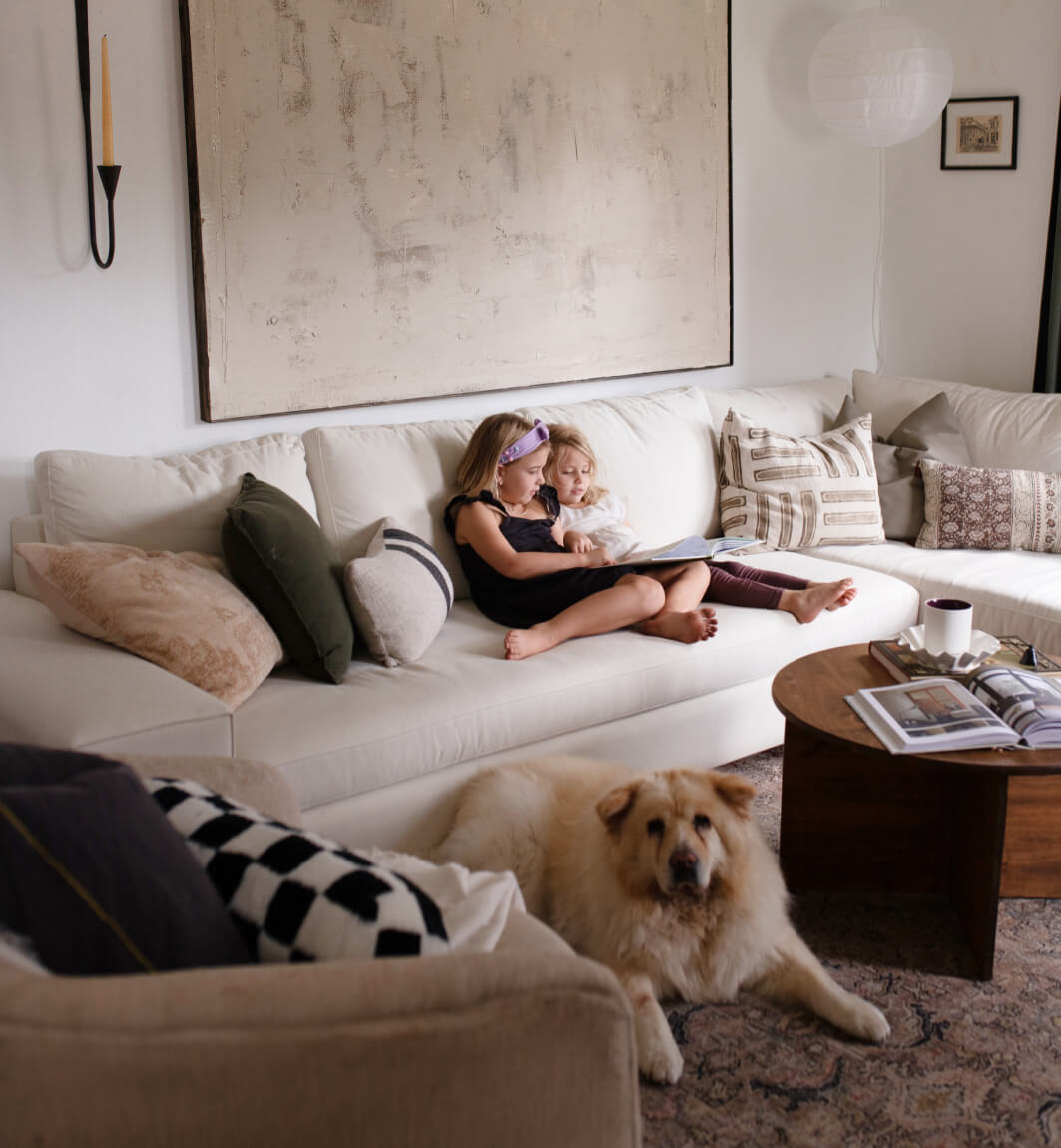 two girls sitting on white sectional near fluffy dog