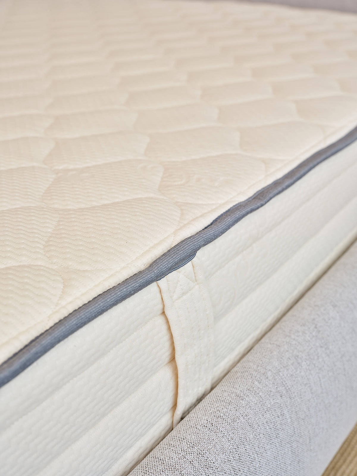 Close-up of cream quilted mattress corner with gray piping